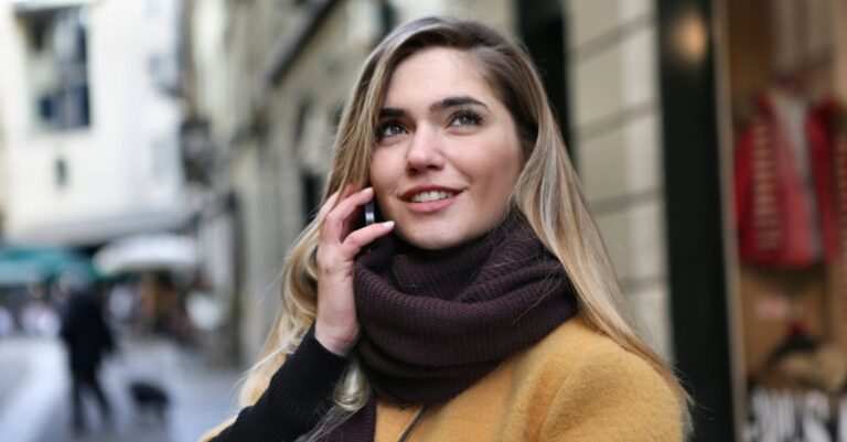 Woman in winter coat and scarf talking on smartphone on a city street.